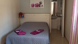 A bedroom with a bed, a bedside table, a mirror, and a bathroom visible through an open door. - Entire private gîte (Lédenon)