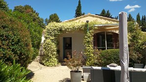 A house with a covered patio, surrounded by greenery and a clear sky. - Entire private gîte (Lédenon)