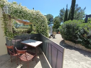 Une terrasse avec une table et des chaises, entourée de verdure et d’une clôture.