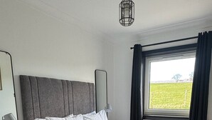 A neatly made bed with white linens, a grey upholstered headboard, and a bedside table with a lamp. - Wallace Lodge - Unique experience (Comrie)