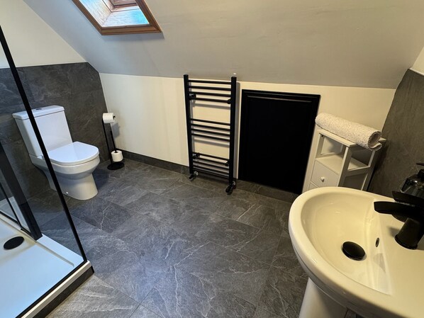A bathroom with a toilet, a sink, a towel rack, and a shower area. - Wallace Lodge - Unique experience (Comrie)
