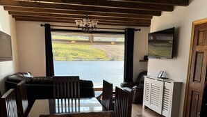 A dining area with a view of a lake, wooden furniture, a TV mounted on the wall, and a cabinet. - Wallace Lodge - Unique experience (Comrie)
