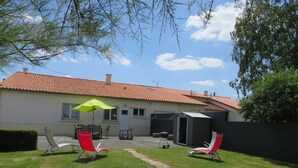 Ein Haus mit rotem Ziegeldach, einer Terrasse mit Gartenmöbeln und einem kleinen Gartenhaus.