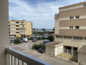 Une vue d’un parking rempli de voitures, d’un immeuble doté de balcons et, au loin, d’une étendue d’eau.