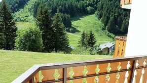 Un balcon donnant sur une vallée boisée et sur un petit bâtiment situé au loin.