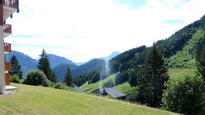 Une maison de campagne avec un toit en pente, entourée de collines verdoyantes et de forêts denses.