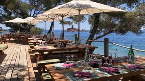 An outdoor dining area with wooden tables and benches, umbrellas, and a view of the sea. - Grand Appartement de 70 m2 vue mer (Saint-Raphaël)