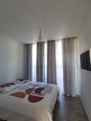 Quarto com cama, cortinas, luminária no teto e televisão na parede.