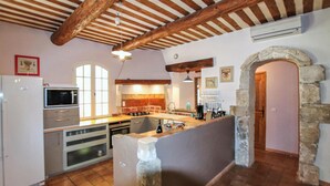 A rustic kitchen with exposed wooden beams, a stone archway, and a tiled floor. - Luxurious home in Apt (Apt)