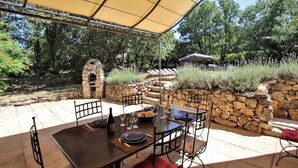An outdoor patio with a stone oven, a table set for dining, and a covered seating area with umbrellas. - Luxurious home in Apt (Apt)