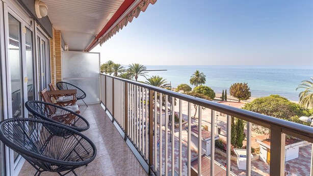 Ein Balkon mit zwei Korbstühlen, einem kleinen Tisch und Blick auf Meer und Strand.