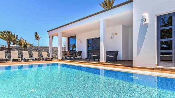 A poolside area with lounge chairs, a covered seating area, and a clear blue pool.