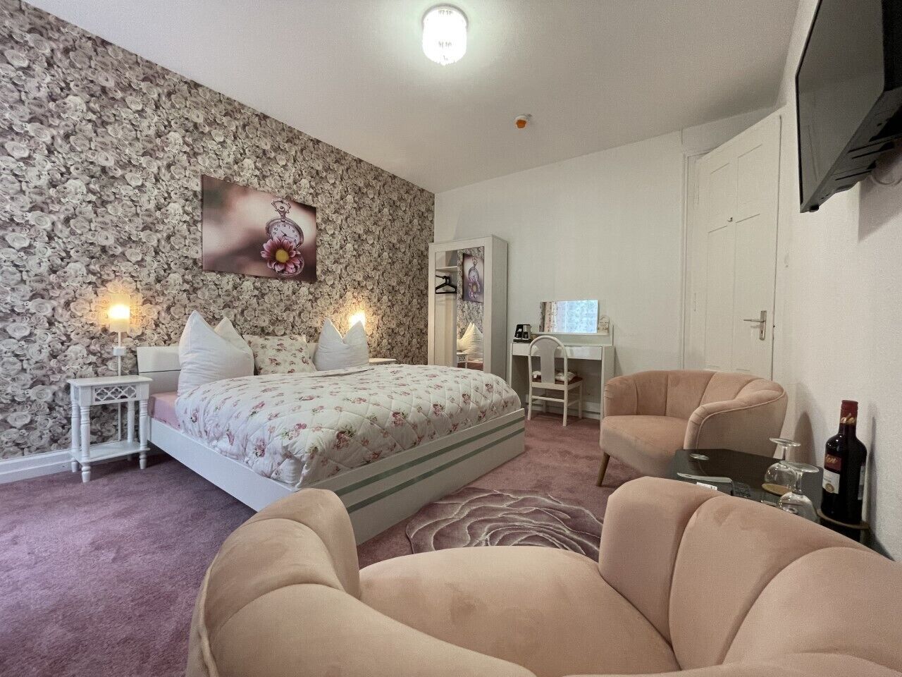 A bedroom with a bed, two chairs, a desk, and a TV.