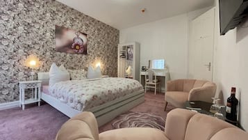 A bedroom with a bed, two chairs, a desk, and a TV.