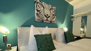 Ein Schlafzimmer mit einer Türkiswand, einem weißen Bett und einem Tiger-Motiv über dem Bett.