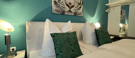 A bedroom with a teal wall, a white bed, and a tiger-themed artwork above the bed.