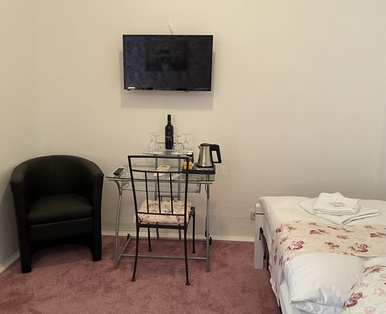 Habitació petita amb un llit, un escriptori amb una cadira, un televisor i una cafetera.