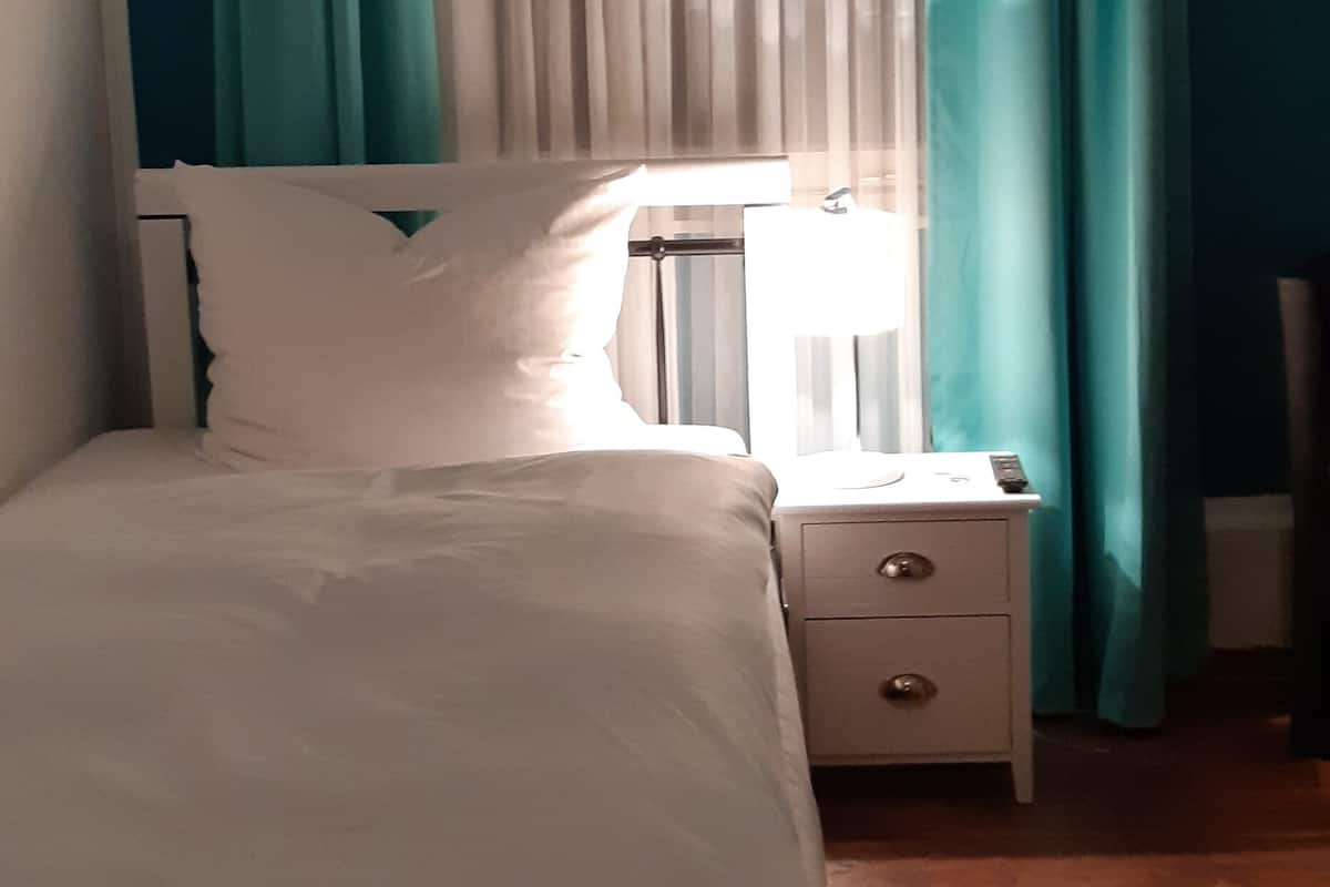 Ein Schlafzimmer mit einem Bett, einem Nachttisch, einer Lampe und Vorhängen.