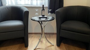 Ein Zimmer mit zwei schwarzen Ledersesseln, einem kleinen runden Tisch, einer Merlot-Flasche, zwei Weingläsern und einer Fernbedienung.