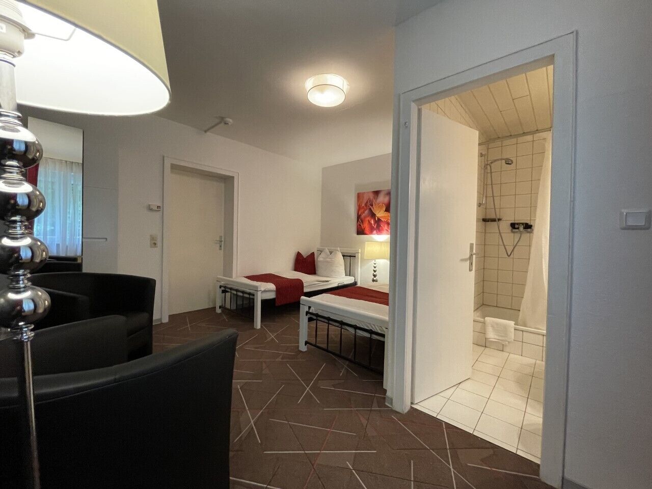 A hotel room with a bed, a desk, a chair, and a bathroom with a shower and toilet.