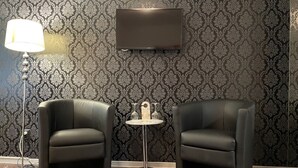 Ein Zimmer mit zwei schwarzen Ledersesseln, einem kleinen runden Tisch mit Weinglashalter, einer Stehlampe und einem an der Wand befestigten Flachbildfernseher.