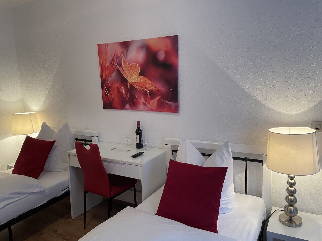 A hotel room with two beds, a desk, a chair, and a painting on the wall.