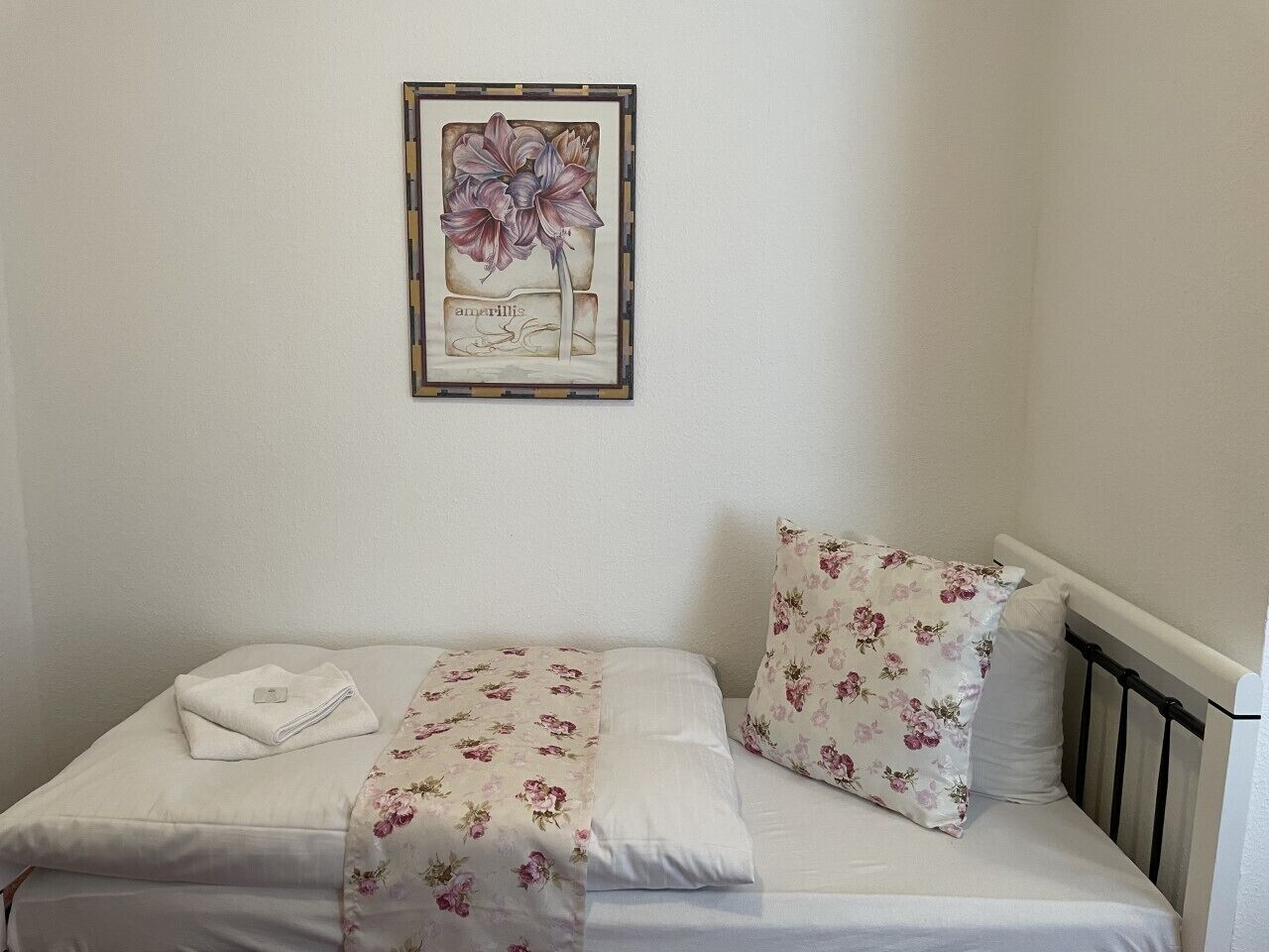 A single bed with floral bedding and a framed botanical print above it.