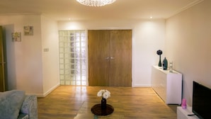 A spacious room with a wooden floor, a chandelier, a wooden door, a white cabinet, and a television. - Stunning Holiday Stay With Free Gym and Parking (Cardiff)