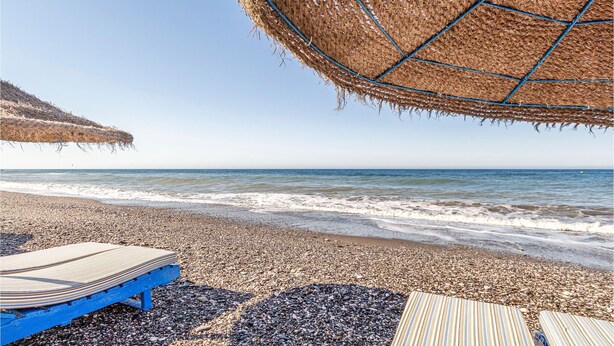 A beach with pebbles, a wooden deck, and a straw umbrella. - Beach front apartment in Torrox Costa with WiFi (Torrox Costa)