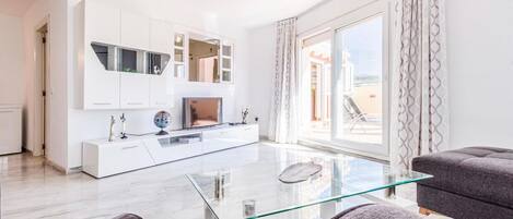 A modern living room with a glass coffee table, a flat-screen TV, and a sofa.