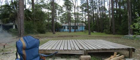 A campsite with a blue cabin, a wooden deck, a fire pit, and a blue folding chair.