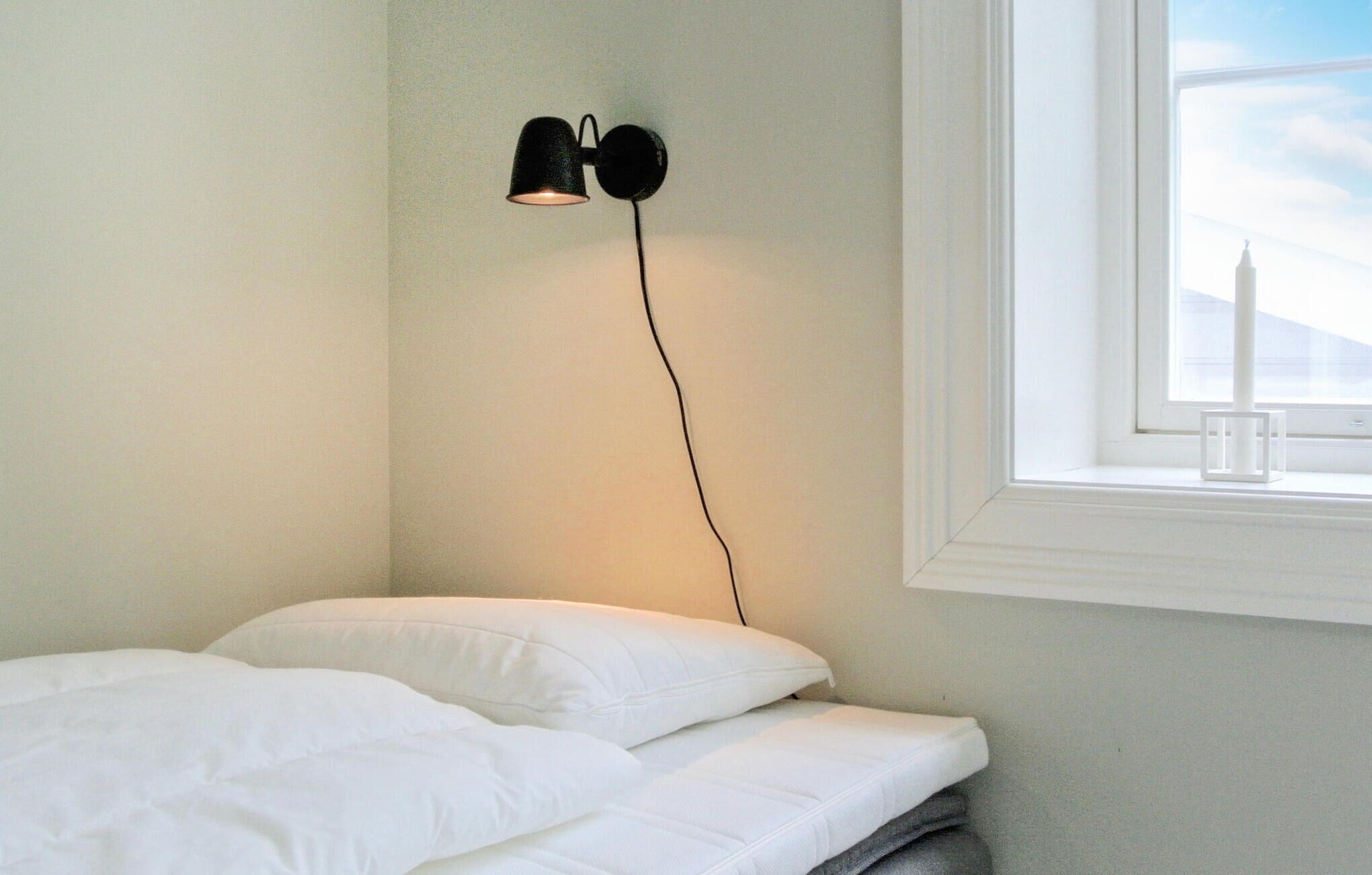 Un dormitorio con cama, mesita de noche, lámpara y ventana con vista a la ciudad.