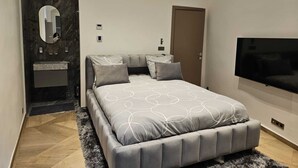 A modern bedroom with a large bed, a built-in TV, a mirror, and a bathroom with a marble wall.