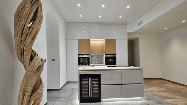 A modern kitchen with a central island, white cabinetry, and a unique wooden sculpture.