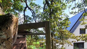 Un banc en bois sous un arbre, un chemin de gravier et un bâtiment avec un toit bleu.