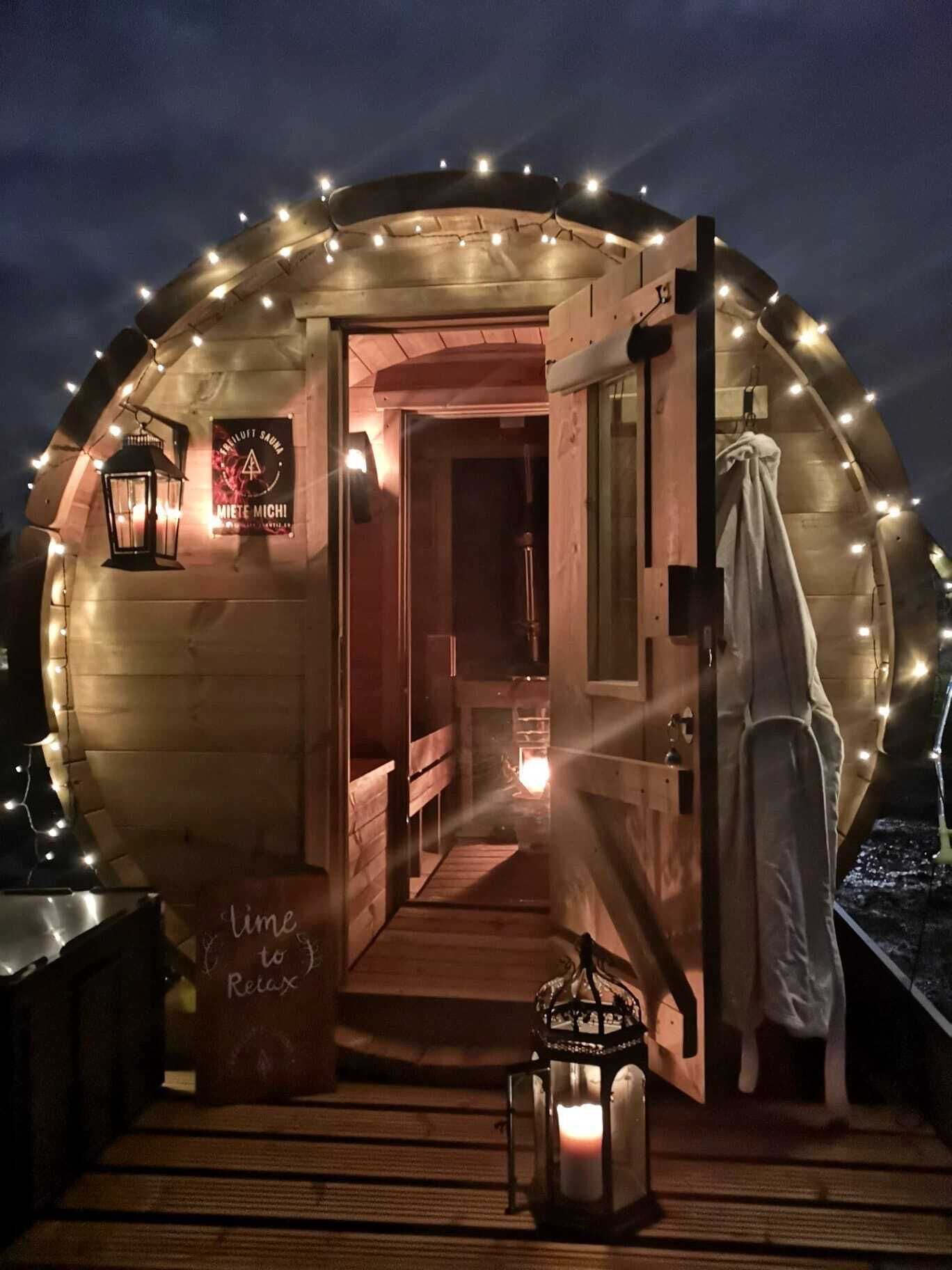 Une structure circulaire en bois, chaleureuse et accueillante, avec une porte donnant sur l’intérieur, illuminée par des guirlandes lumineuses.