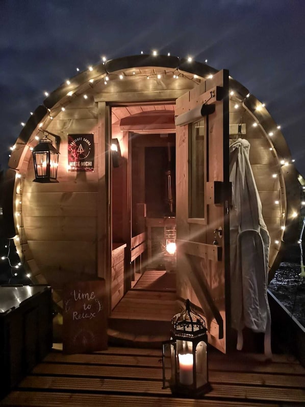 A cozy, circular wooden structure with a door leading inside, illuminated by string lights.