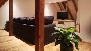 Un salon chaleureux avec un canapé foncé, des poutres en bois, un téléviseur à écran plat et une plante en pot.