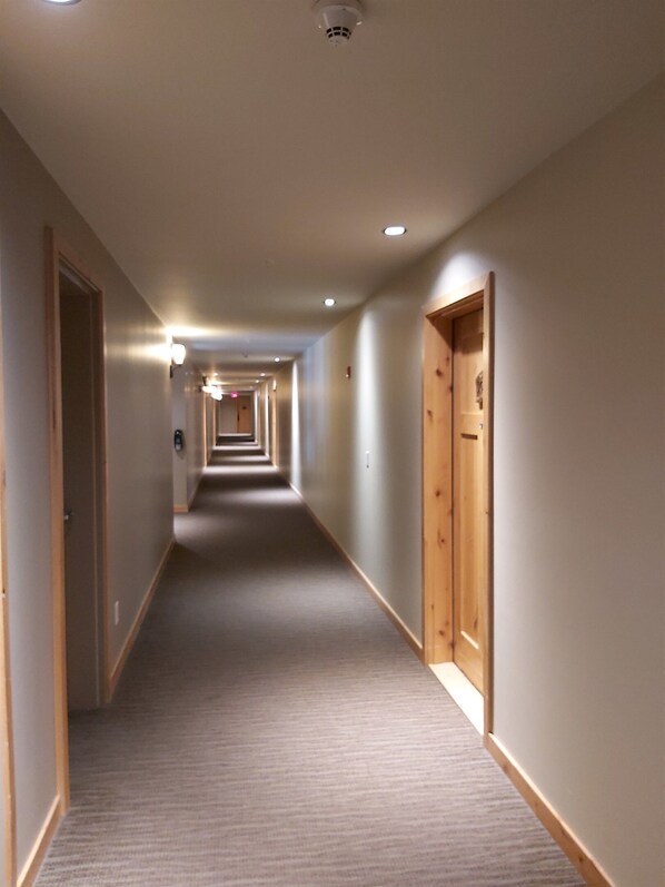 Un long couloir étroit, dont le sol est recouvert de moquette et où l’on trouve des portes en bois de chaque côté.
