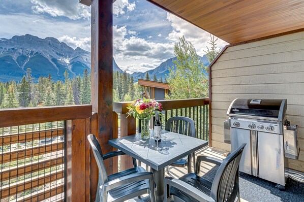 A balcony with a table set for two, a grill, and a view of mountains.