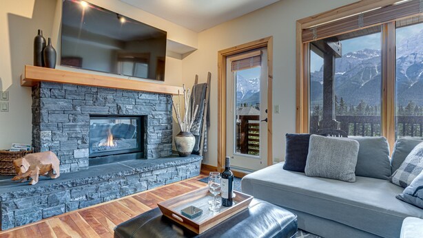 Ein gemütliches Wohnzimmer mit Kamin aus Stein, einem großen Fenster mit Blick auf die Berge und einer bequemen Sitzecke.