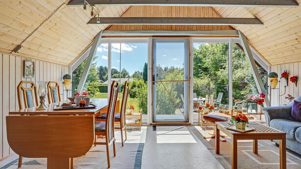 Amplia habitación con un gran ventanal corredero que da a un jardín, muebles de madera y vistas al exterior.