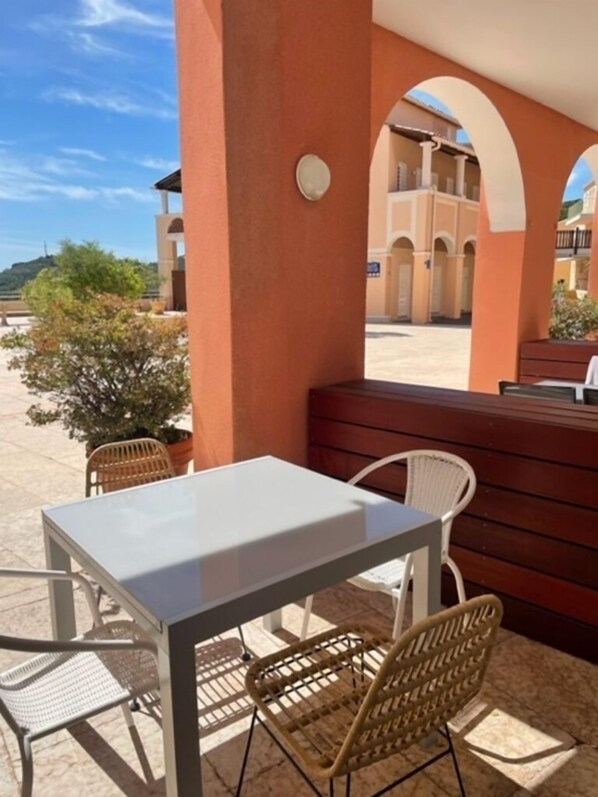 Un espace extérieur aménagé avec une table et des chaises, un banc en bois et une vue sur un bâtiment doté d’arcades.