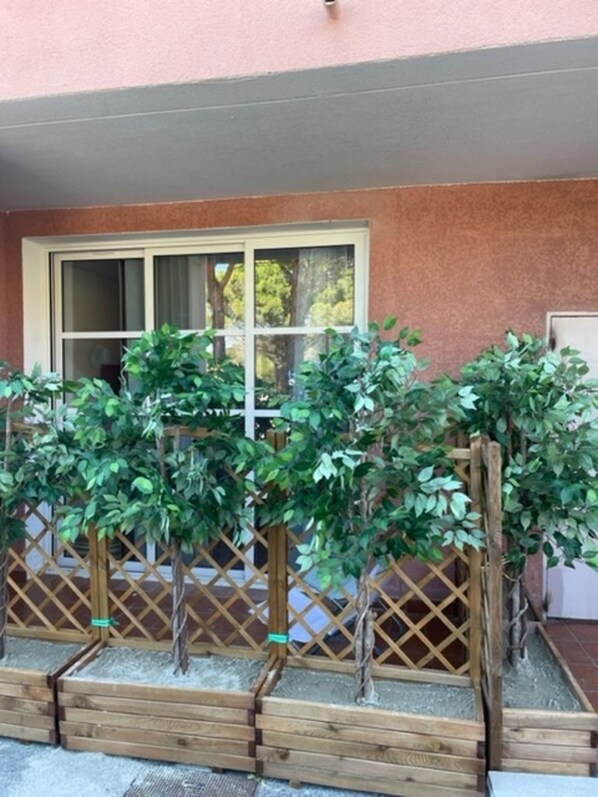 Una celosía de madera con plantas verdes frente a un edificio con una ventana y una puerta.