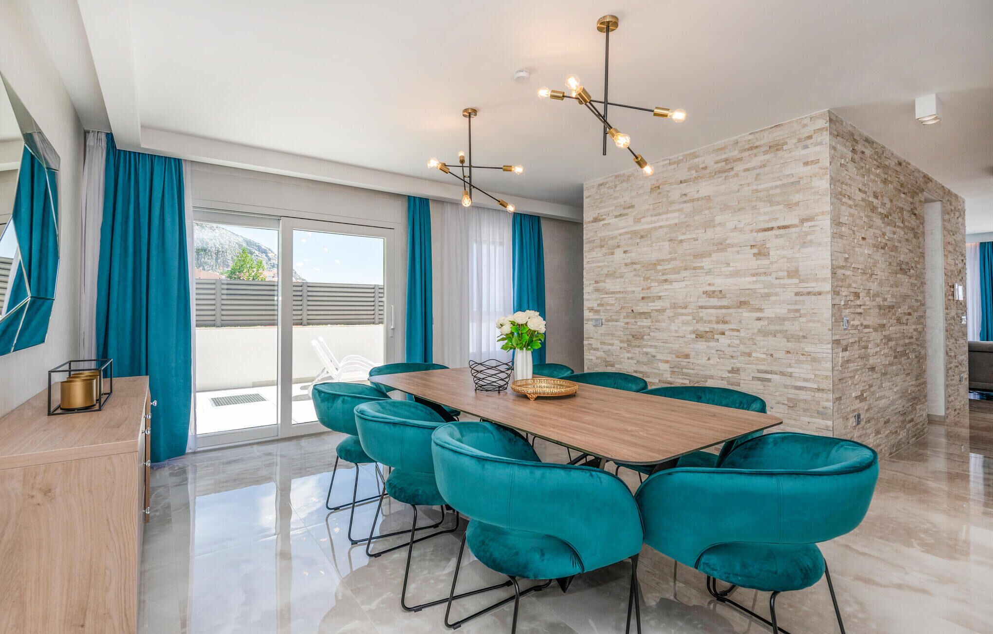 A modern dining area with a wooden table, teal chairs, and a stone accent wall.