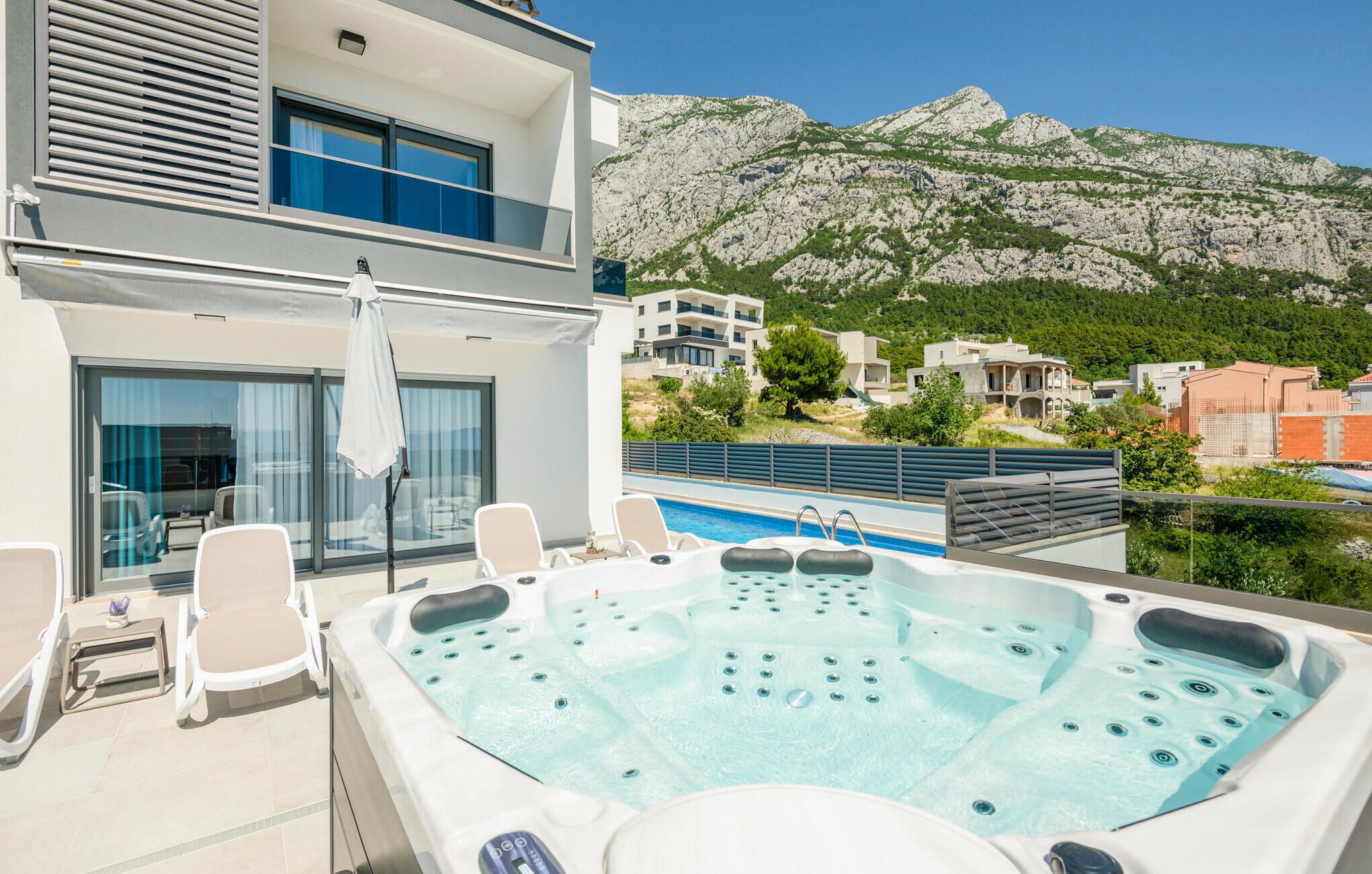 Un área de piscina en la azotea con un jacuzzi, sillas de descanso y vistas a un paisaje montañoso.