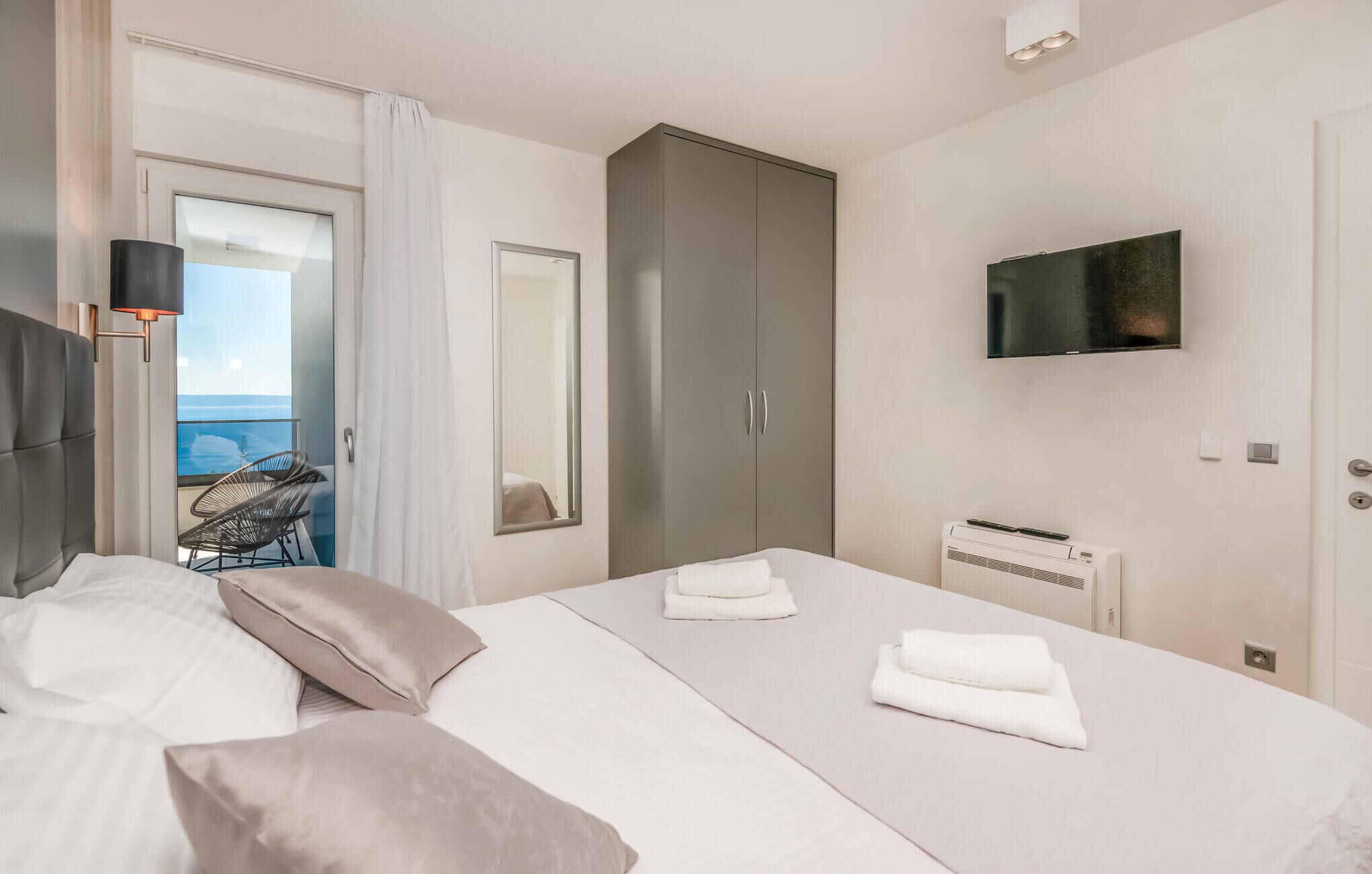A modern hotel room with a bed, a wardrobe, a TV, and a view of the sea.