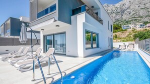 A modern poolside area with lounge chairs, a clear blue pool, and a mountain backdrop. - Lovely home in Makarska (Makarska)