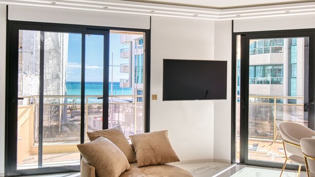 Una sala de estar moderna con un ventanal grande, un televisor de pantalla plana y un sofá color beige.
