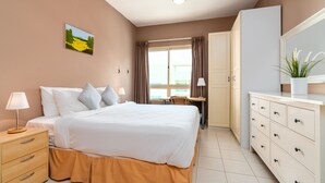 Habitación de hotel con cama, mesita de noche, lámpara, armario y ventana con cortinas.